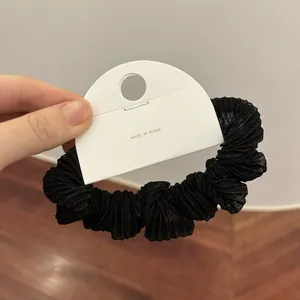 Detail van een geplooide zwarte scrunchie met zijdeachtige textuur en Koreaanse verpakking