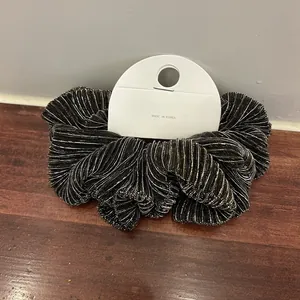 Detail of elegant black pleated hair scrunchie with silver glitter stripes on display card
