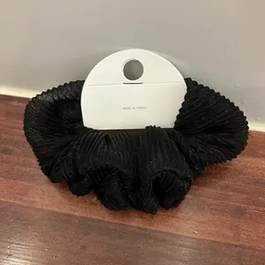 Close-up of black pleated fabric hair scrunchie with metallic sheen on display card