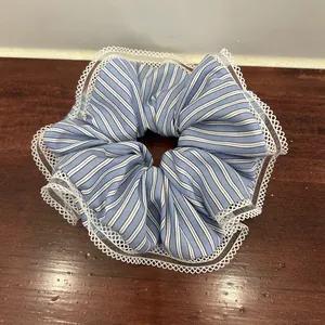 Detail of striped blue fabric scrunchie with layered white lace trim on wooden background