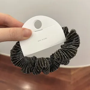 Detailopname van zwarte scrunchie met metallic glans en witte kartonnen verpakking