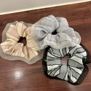 Close-up of three striped fabric scrunchies with sheer organza lace edges on wood