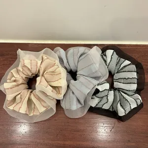 Detail of three striped organza hair scrunchies with mesh lace edges on wood