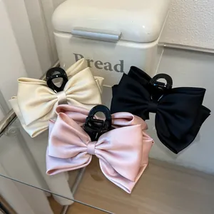 Detail of large satin bow hair claws in beige pink and black with glossy texture