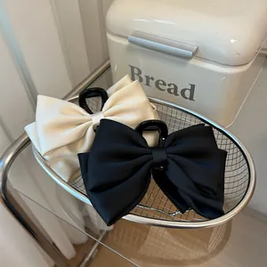 Detail view of large satin bow hair claws in black and beige within a wire basket