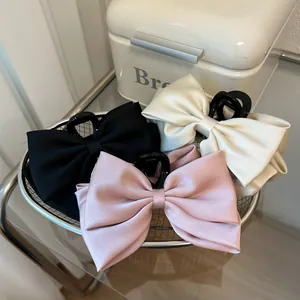 Macro view of large satin bow hair claws in black, cream, and pink in a metal basket