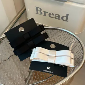 Detalle del juego de pinzas para el cabello con lazo de satén en negro y crema