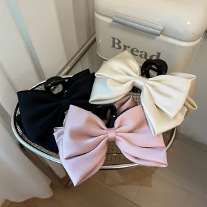 Three large satin bow hair claws in black, beige, and pink with a silk finish