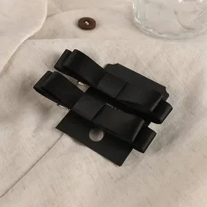 Primer plano de dos horquillas con lazo de satén negro sobre tarjeta en fondo de lino