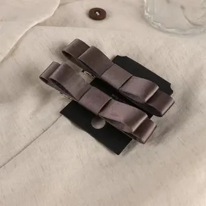Detalle de pinzas para el cabello con lazo de satén marrón oscuro en un fondo de tela