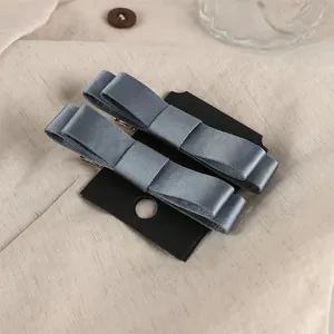 Detalle de horquillas con lazo de satén azul grisáceo sobre fondo de lino natural