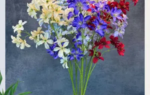 Bouquet de clématites artificielles aux pétales bleus, violets et rouges sur mur gris