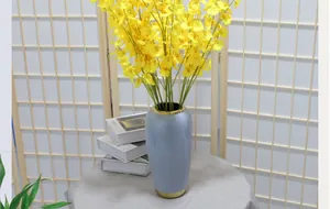 Close-up of artificial dancing lady orchids in a blue ceramic vase with gold rim detail