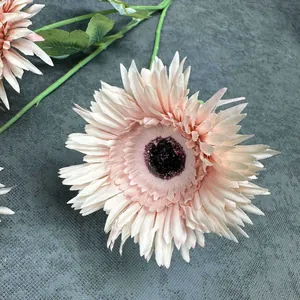 Gerbera artificiale rosa con tre teste di fiori e foglie verdi su panno grigio
