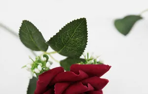 Macro detail of red velvet artificial rose petals and green textured leaves with berries