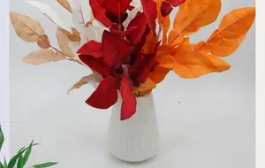 Detailed view of artificial pomelo leaves in warm autumn colors in a white vase
