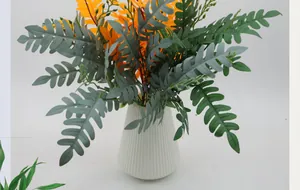 Close-up of artificial fern leaves in orange and grey-green with a white striped vase