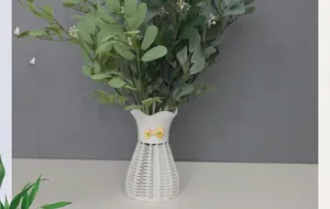 Close-up of artificial green leaves in a white woven texture vase with a yellow bow