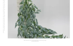 Détail de plante de saule artificiel gris-vert dans un pot blanc minimaliste à rayures