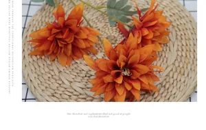 Three-headed orange artificial dahlia flowers on a woven mat with a checkered cloth