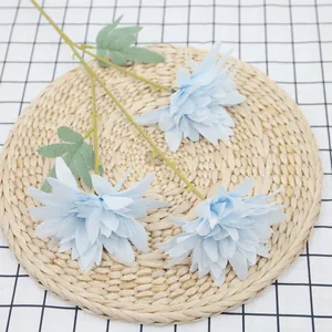 Three stems of light blue artificial dahlia flowers on a straw mat for home decoration