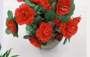 Detalle de azaleas rojas artificiales con pétalos de seda en un jarrón gris texturizado