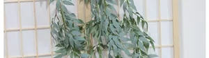 Close-up of artificial hanging willow leaves with natural grey-green texture on wood