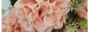 Macro shot of realistic silk hydrangea petals in soft peach pink with green leaves