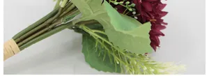 Close-up of artificial burgundy daisies with realistic green leaves and raffia binding