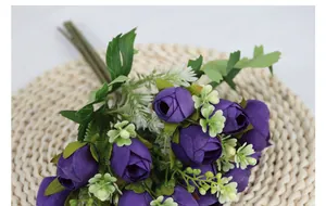 Close-up of deep purple artificial silk rose buds with green leaves on a woven mat