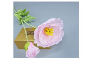 Close-up of pink artificial poppy with pleated petals and yellow stamens on a golden box