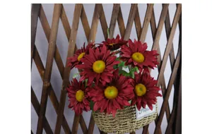 Hanging basket with dark red artificial sunflowers on a rustic wooden trellis fence