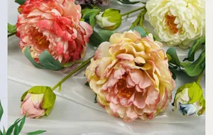 Detailed close-up of faux peonies with realistic silk petals and green leaves on silk cloth