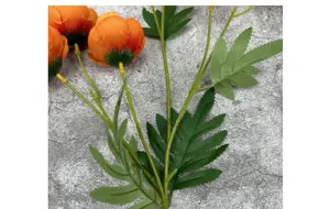Primer plano de flores de camelia artificiales naranjas con hojas verdes en fondo gris