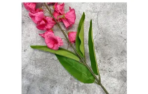 Close-up of pink artificial lily of the valley branch with green leaves on grey background