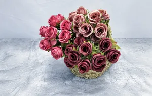 Close-up of artificial rose bouquet with pink and red silk flowers in a woven basket