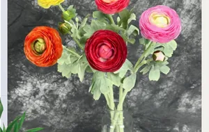 Detailed view of colorful faux ranunculus flowers with flocked stems in a glass vase