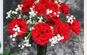 Detail of red faux carnations and baby's breath flowers in a dark glass vase