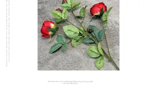 Macro shot of artificial red silk roses with realistic green leaves on grey background