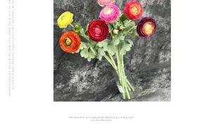 Vibrant faux ranunculus silk flowers in glass vase with yellow orange and pink blooms
