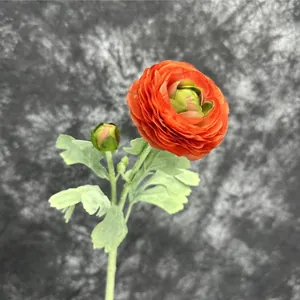 Artificial ranunculus flower with orange petals, green foliage and bud in a close-up shot