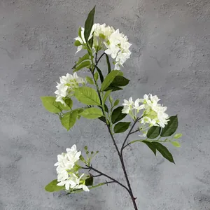Artificial white lilac bouquet with realistic green leaves against a grey wall