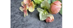 Close-up of silk peach rose buds and yellow lily petals with detailed green leaves