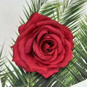 Draufsicht einer tiefroten Seidenrosenblüte auf einem grünen Palmenblatt-Hintergrund
