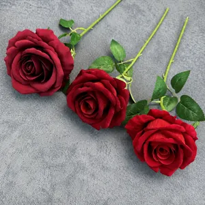 Three realistic velvet artificial roses in burgundy, dark red, and bright red on grey fabric