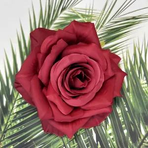Testa di rosa artificiale in seta rosso intenso su sfondo di foglie di palma