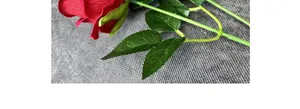 Primer plano de rosas de terciopelo rojo artificial con hojas verdes sobre fondo gris