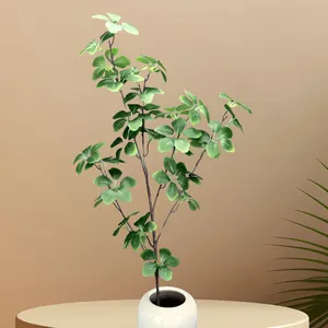 Detail of artificial green foliage in white ceramic vase on light wood table