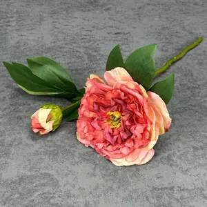 Pink artificial peony flower with realistic gradient petals and green leaves on gray cloth