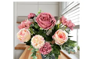 Dettaglio di un bouquet di rose e peonie artificiali con foglie verdi su tavolo di legno